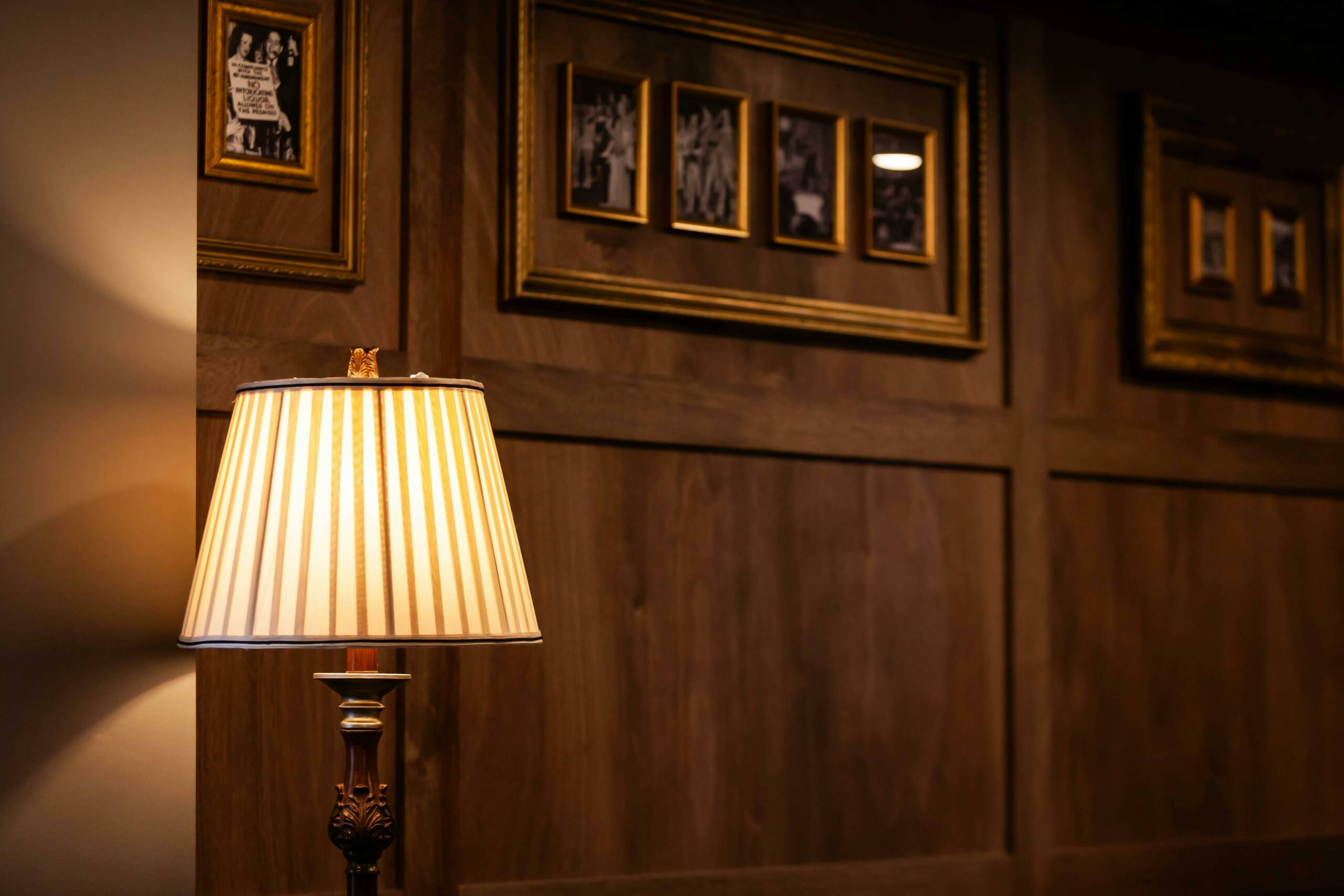 A lamp in front of a wooden panelled wall with historical photographs and art