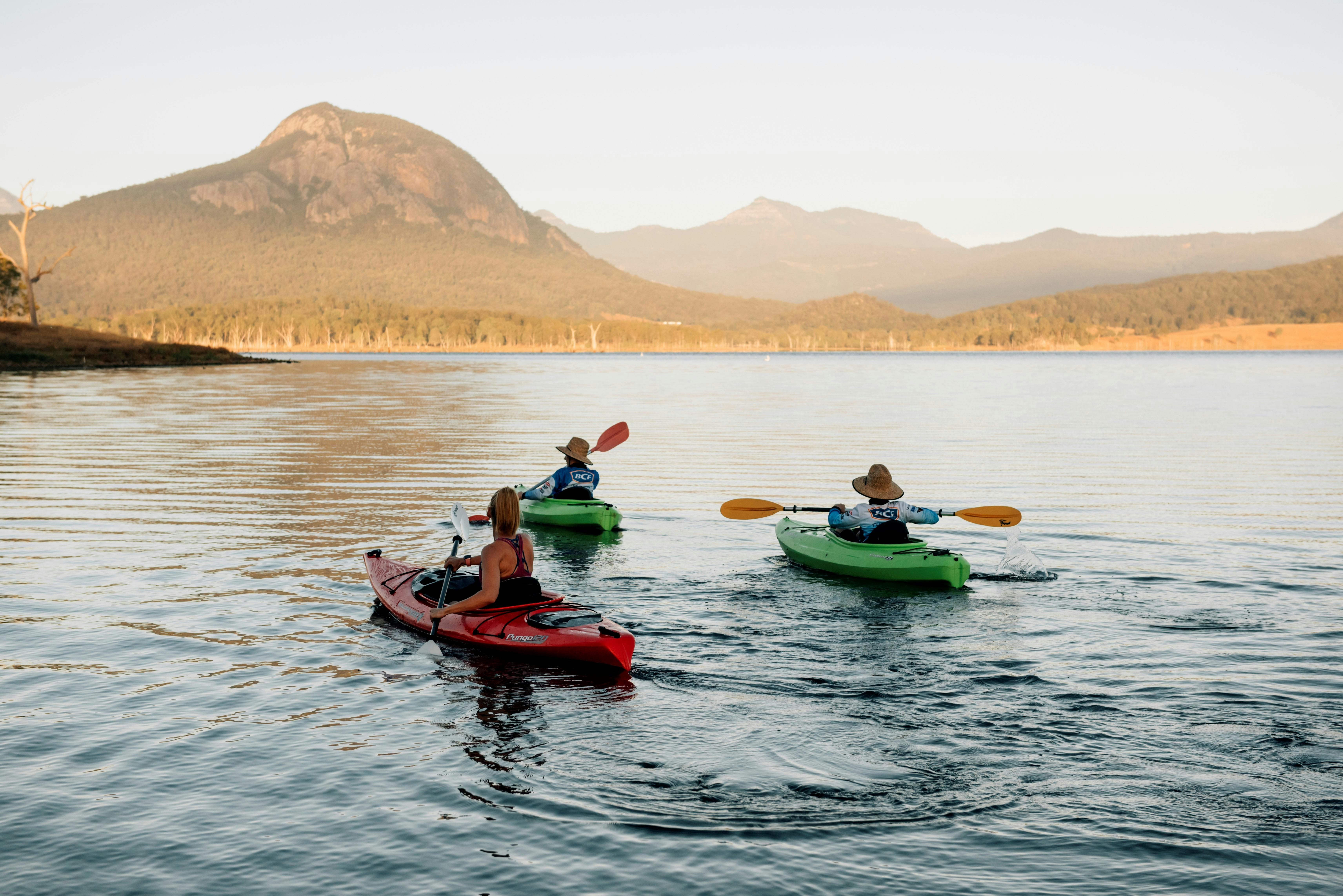 Three people kayak across a lake towards a distant mountain range